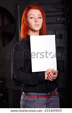 Woman hold blank paper sheet, standing on a dark background. Girl holding a large white sheet as the place for inscriptions. Advertising message that will keep a woman in his hands.