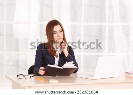 Woman student or beginner office staff at work in the office. She works at his laptop beech and makes notes in a notebook. The girl secretary or office manager sitting at the table on time of the day.