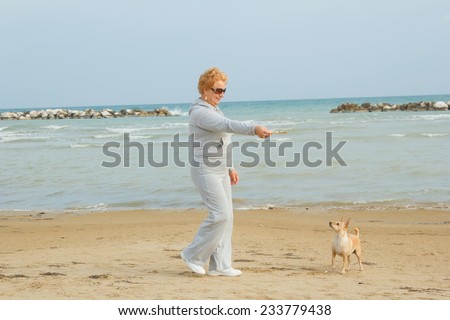Adult woman walking with a dog on a sea beach. Walking with a pet. Dog - a friend of pensioners. Beach, sea, animals, walk, ocean, fresh air, the resort - the concept of lifestyle old woman retired.