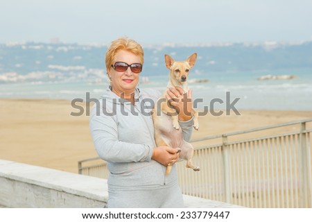 Adult woman walking with a dog on a sea beach. Walking with a pet. Dog - a friend of pensioners. Beach, sea, animals, walk, ocean, fresh air, resort - the concept of lifestyle old woman retired.