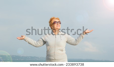 Adult woman on the background of the sea. Senior woman in tracksuit enjoying life. Fitness classes in the open air near the sea and the beach. Lifestyle adult retired.