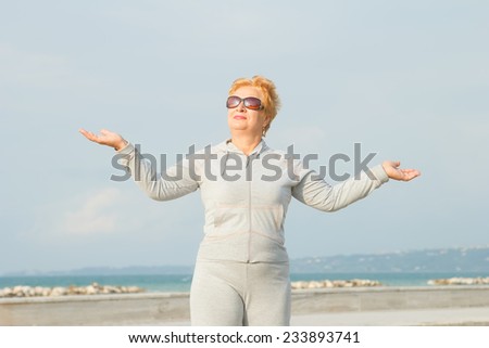 Adult woman on the background of the sea. Senior woman in tracksuit enjoying life. Fitness classes in the open air near the sea and the beach. Lifestyle adult retired.