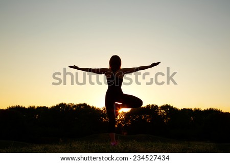 Silhouette of a woman at sunset or sunrise. Woman open arms under the sunrise. Woman doing yoga outdoors at sunset. Modern girl doing fitness exercises.