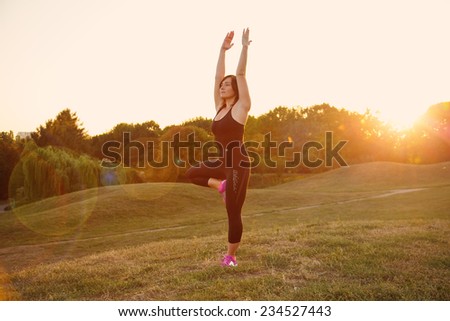 Woman open arms under the sunrise. Woman doing yoga outdoors at sunset. Modern girl doing fitness exercises. Aura, silhouette, health, sport, fresh air, park - concept of relaxation modern woman.