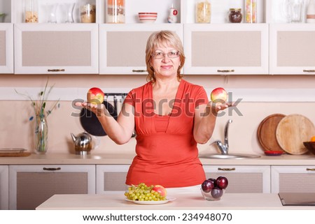 Woman preparing fruit in the kitchen. Adult woman holding fresh fruit. Happy woman holding plate full of fruits in the kitchen background. Apples, plums, grapes - kitchen stories are preparing food.