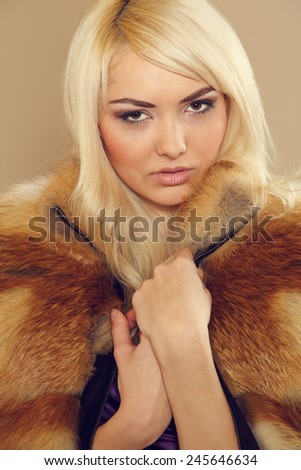 Blonde woman wearing a fur coat. Coat of fox fur wearing a beautiful woman. Red fur. Girl showing makeup on her face. Concept for advertising winter clothing. Beautiful luxury winter woman in fur coat