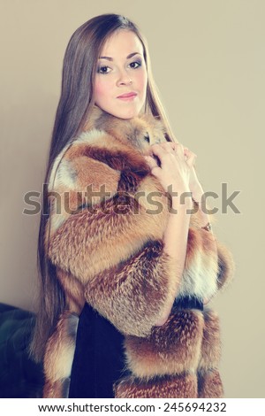 Brunette woman wearing a red fur coat. Beautiful luxury winter woman in fur coat. Coat of fox fur wearing a beautiful woman. Girl showing makeup on her face. Concept for advertising winter clothing.