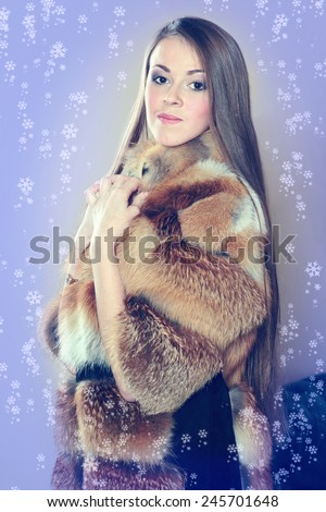 Beautiful luxury winter woman in fur coat. Brunette woman wearing a red fur coat. Coat of fox fur wearing a beautiful woman. Girl showing makeup on her face. Concept for advertising winter clothing.