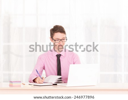 Man in business attire working at a laptop. Employee of the office. Student are trained in the office. Work with documents and computer. Trainee working in the office. Young man assistant manager.