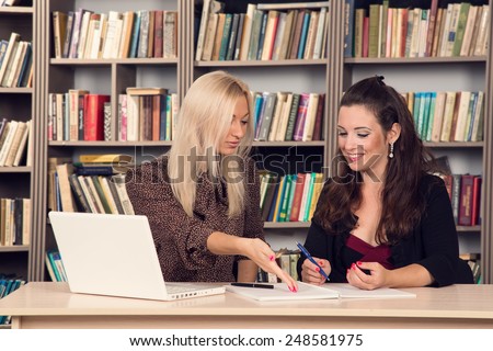 Conversation women office. Two young businesswomen having a meeting in the office sitting at a desk having a discussion with focus. Two girls students discuss course material. Work on the computer.