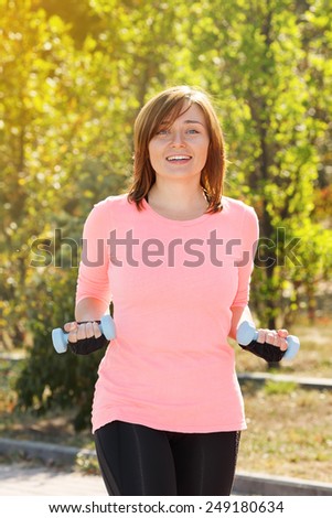 Young woman holding a dumbbell for fitness. Woman involved in sports and fitness in nature. Sports fitness outdoors. Active lifestyle urban dweller. Exercise at the city park. Fitness instructor.
