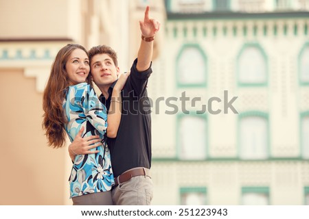 Man points a finger at hand in the direction of something interesting. Love story man and woman who travel to city. Man embraces woman and she is very happy. Joy, love is mutual feelings of two people