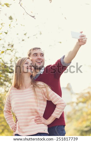 Do yourself a photo. Loving couple photographed together on a mobile phone. Happy couple in love taking self-portrait photo on City Park. Young tourists having fun date. Asian man, caucasian woman.