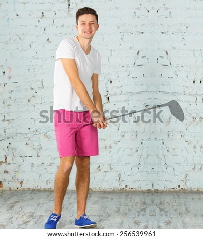 Dream of playing golf. Dreams come true. Male athlete in a white shirt and pink shorts on the brick wall background. Modern young man. Silhouette of a golf club in his hands. Get credit for dreams.