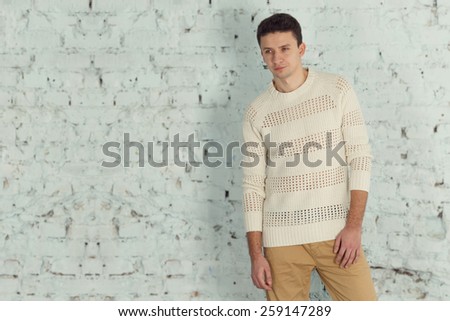 Stylish male model in a white jacket. Portrait of handsome caucasian brunette. Young modern man stands on a light background of a brick wall. American, European who works as a model. serious cheerful