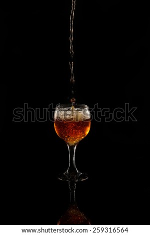 Glass goblet on a black background. In a glass of beer or wine is poured. Jet of liquid fills the glass. A glass of dark honey beer. Amber glass of wine. Pour into a glass, pour a full.