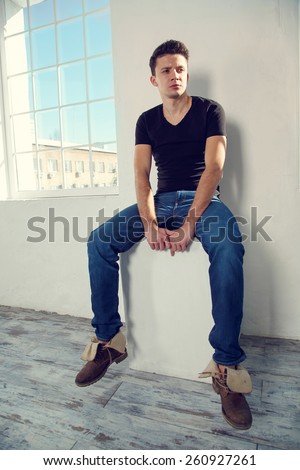 Modern male model posing on light background next to the large windows. Man are in the room near the window light. Handsome man in free space. The concept for the design and advertising.