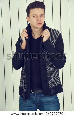 Male model posing on a light background of wood. Portrait of young beautiful fashionable man against wooden wall. Jeans fashion man with short dark hair. Wearing blue jeans, jacket.