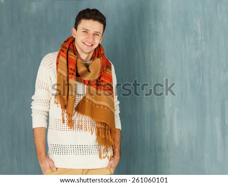 A young man with a beautiful smile. A man in a good mood. Learn the good news and be happy. A man with a white jacket with a scarf around his neck on a background of gray wall. Space for text.