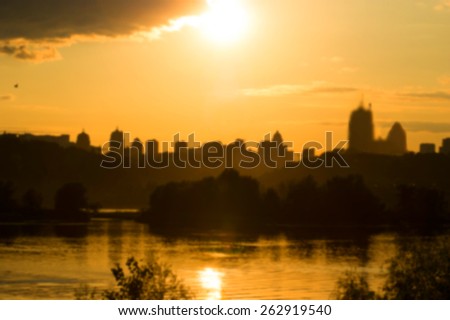 Sunset on the city background. Silhouette of the city in the rays of the evening sun light. Blurred image of a photo of the city. View of the city from the other side of the river. Ukraine, Kyiv city