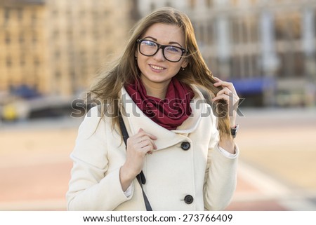 Young modern beautiful woman. Stylish woman in a bright coat and glasses on his face. Woman on the background of the city at sunset the sun. Get out of the office after work. Girl student. Red scarf.