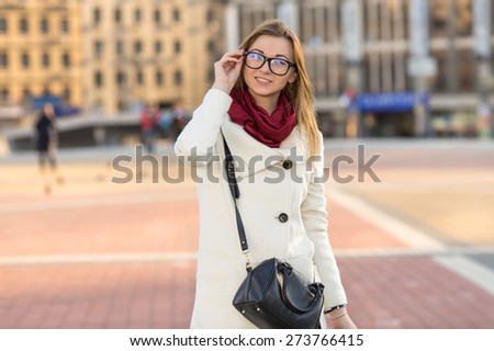 Young modern beautiful woman. Stylish woman in a bright coat and glasses on his face. Woman on the background of the city at sunset the sun. Get out of the office after work. Girl student. Red scarf.
