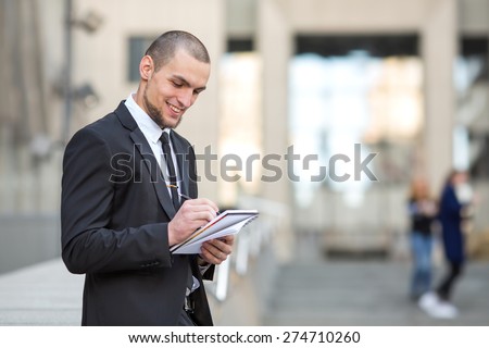 Modern businessman. Young man of arabic origin in a suit. Business man in the background office building. Confident businessman portrait. Confident and charismatic modern business man. Note pad record