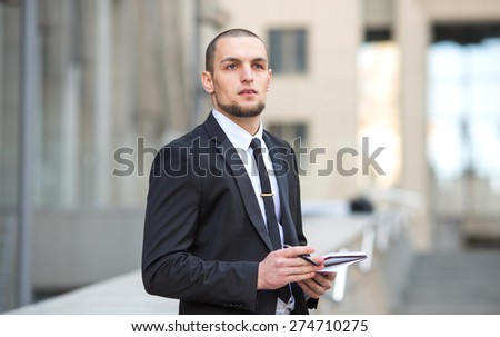 Modern businessman. Young man of arabic origin in a suit. Business man in the background office building. Confident businessman portrait. Confident and charismatic modern business man. Note pad record