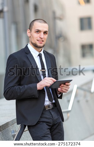 Business man and tablet computer. Businessman using his tablet on the background of office building. Young male executive using digital tablet against blurred background. Business hours. Work near.