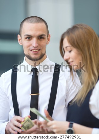 Man receiving money, US dollars. Business man holding a money hundred dollar banknotes. Businessman and businesswoman on blurring background office building work. They count the money and divide.