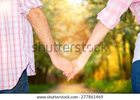 Blurred image of the hands of a loving couple in the sun light. Blurry background image for the text about love. Young couple hold each other\'s hands summer on sunny park background. Love Story