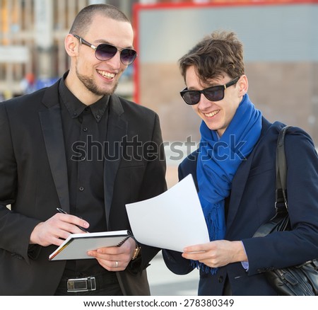 Business meeting. Two businesspeople looking at papers. Two modern business man discussing business documents and contracts in hand. Men in the business center on the background of an office building.