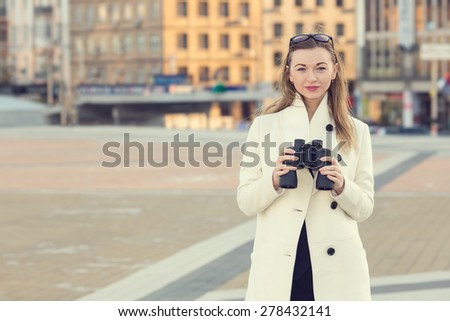 Woman and binoculars. Business woman with binoculars in his hand against the background of the streets downtown. Businesswoman holding binoculars. Concept - looking for a job. Young girl with spying.