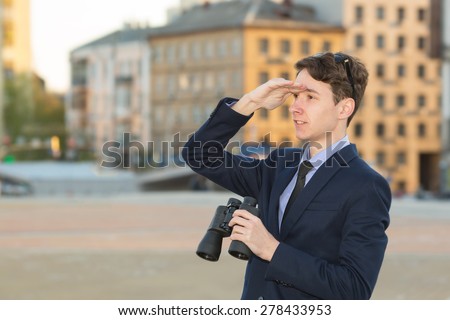 Man and binoculars. Business man with binoculars in his hand against the background of the streets downtown. Man holding binoculars. Concept - looking for a job. Man with spying. Service monitoring.