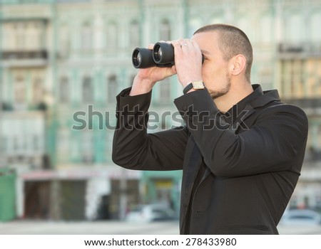Man and binoculars. Business man with binoculars in his hand against the background of the streets downtown. Security man holding binoculars. Looking for a job. Man with spying. Service monitoring.