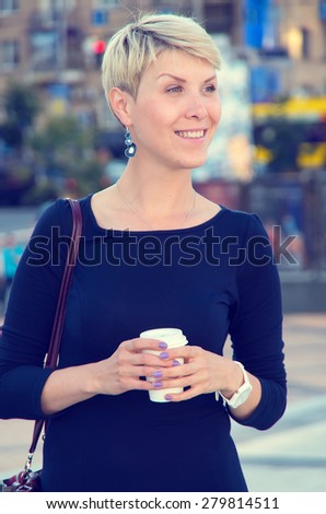 Business woman on a city street. Drink a cup of tea or coffee in the office do not. Small business. Woman dreams. She took a break in the work schedule. Going home from the office.
