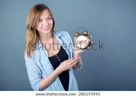 Woman watches and time. Woman holding a clock. Young modern girl on a blue background. Ordinary young european girl with an alarm clock in his hands. Girl student indicates the time on the clock.
