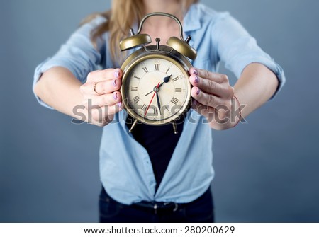Woman, clock and time. Woman holds before itself in the hands of the clock. Only hands clock close-up on a blue background. European woman with an alarm clock in his hands. Girl shows at the clock.