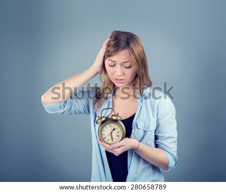 Stress - woman stressed with headache. Surprised woman with alarm clock on blue background. Female stressed and worried with migraine headache pain. Thirty minutes after the two. Afternoon.