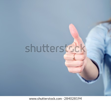 Thumb up. Women\'s hand shows the sign that everything is fine, everything is very good. Woman thumb up on blue background. Space for text. Left, right. Concept about the good things and the good news.