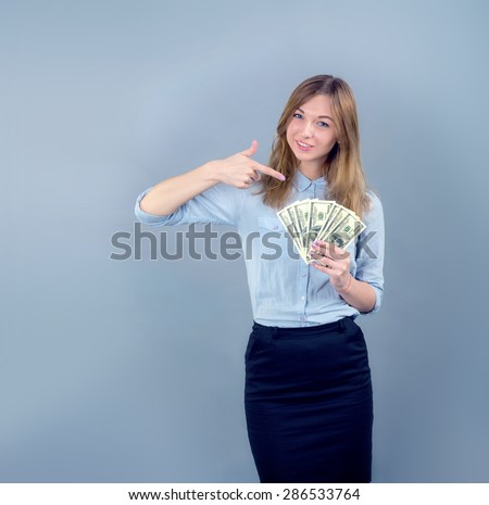 Business woman smiling and pointing finger to money on grey blue background. Woman pointing at USA notes. Young woman holds the money US dollars. Save for study. Girl student to receive a scholarship.