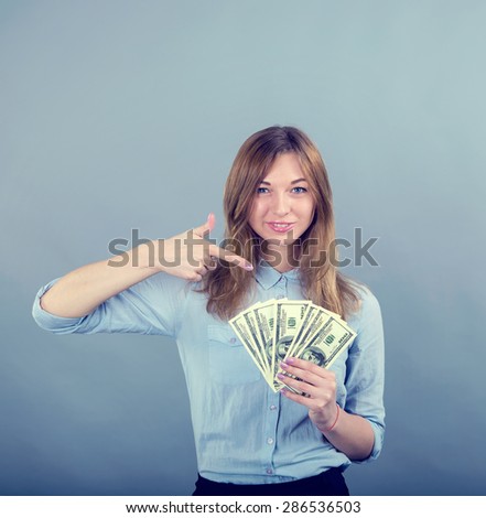 Business woman smiling and pointing finger to money on grey blue background. Happy young woman hold money dollar bills in hand. Positive emotion facial expression feeling. Financial reward. Woman USA.