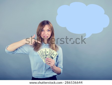 Business woman smiling and pointing finger to money on grey blue background. Woman pointing at USA notes. Young woman holds the money US dollars. Place for advertisement message. To receive a income.