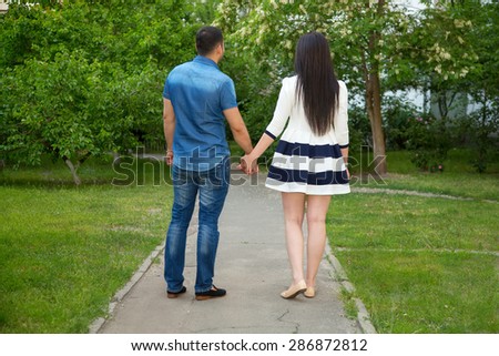 Love Story. Man, woman together. Multiracial couple in love. Walk a summer day in the city or in the park where the many green plants. Trips after the wedding. Hold hands together. View from the back.