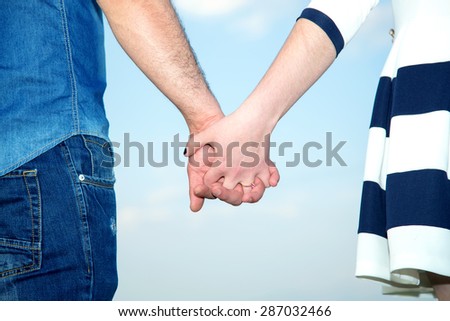 Clasped hands of a young romantic man and woman against a blue sky with copy space. Conceptual image of love, friendship. Love Story. Concept shoot of friendship and love of man and woman: two hands