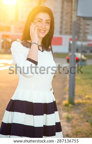 Woman talking on the mobile phone. It is against the backdrop of the city in the rays of sunset. Woman of Asian appearance is in the rays of a sunset on the background of urban buildings. Azerbaijan