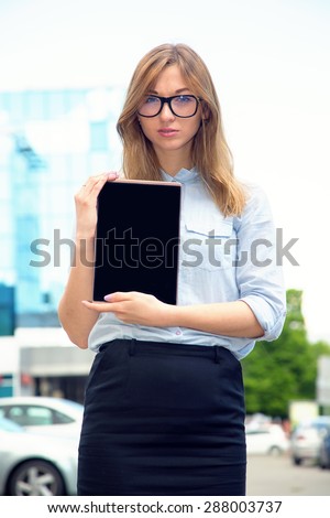 Beautiful woman spectacled holding digital tablet. Female student using touch pad against city background. Freelancer girl working on her digital tablet. Woman browsing with touchscreen device,