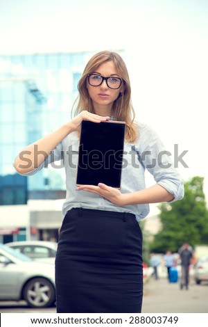Beautiful woman spectacled holding digital tablet. Female student using touch pad against city background. Freelancer girl working on her digital tablet. Woman browsing with touchscreen device,