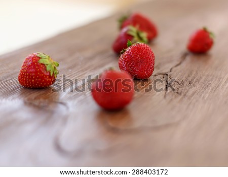 Strawberries on a wooden table. Focus on the berry which is at the center of the table. Other berries like blurred. Blurred image of strawberries.