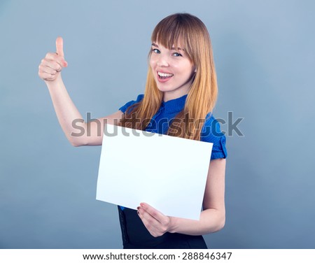 Happy woman holding a white banner and smiling. Woman hold white paper banner. Young smiling woman show blank board. Female model portrait on blue background. Concept - insert labels, ads. She shows.